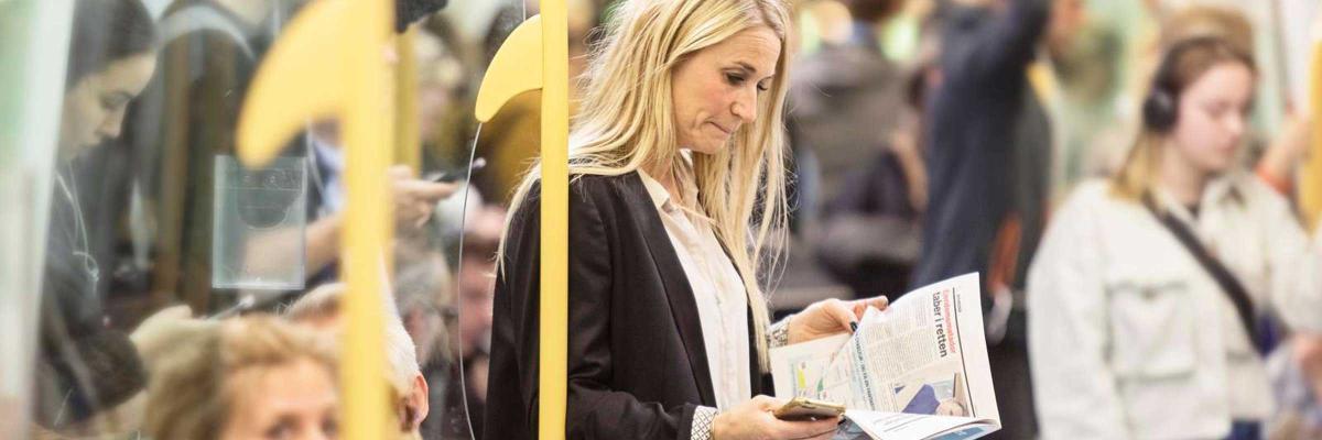 En kvinna står och läser tidningen i metrotåget